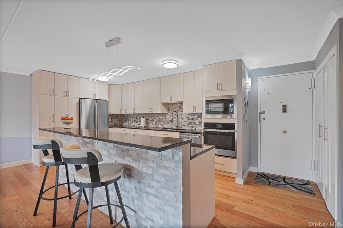 Kitchen featuring appliances with stainless steel finishes, ornamental molding, pendant lighting, light wood-type flooring, and tasteful backsplash