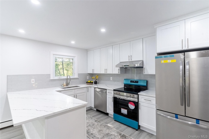 Kitchen featuring appliances with stainless steel finishes, white cabinetry, light stone counters, and recessed lighting