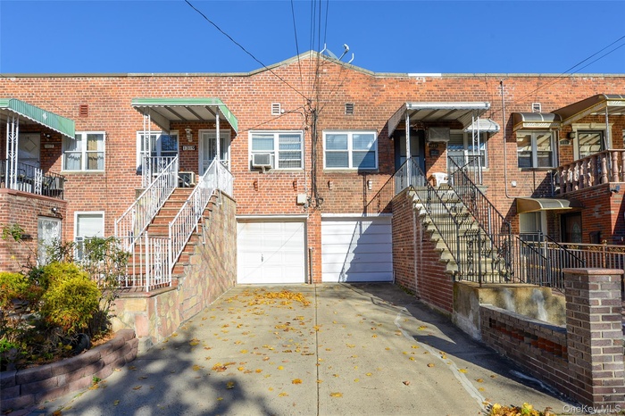 Back of property with concrete driveway, an attached garage, brick siding, and stairway
