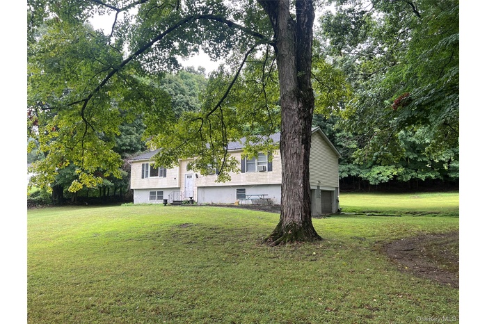 View of front facade with a front lawn, a garage, and view of scattered trees