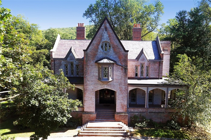 View of front facade featuring covered porch, brick siding, a chimney, and a high end roof