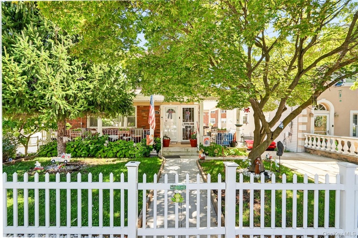 View of property hidden behind natural elements with a fenced front yard, brick siding, and a gate