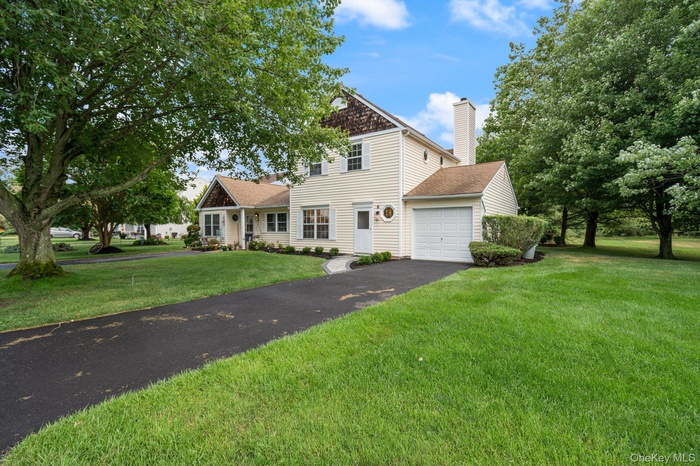Traditional-style home with a garage, driveway, a chimney, a front lawn, and a shingled roof