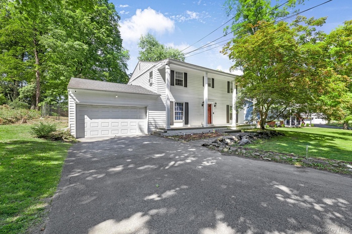 Colonial home with a front yard, an attached garage, driveway, a shingled roof, and a porch