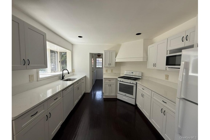 Kitchen featuring white appliances, dark wood-type flooring, custom exhaust hood, and light stone countertops