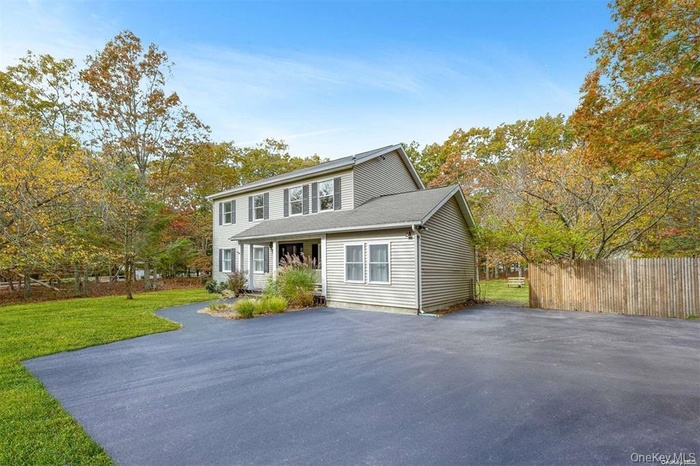 View of front of property with asphalt driveway, roof with shingles, and view of wooded area