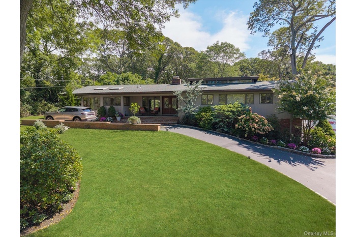 View of front facade with a front lawn, a porch, a chimney, brick siding, and view of scattered trees