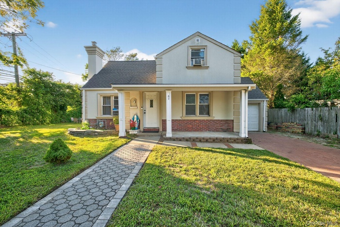 Traditional-style home with brick siding, stucco siding, covered porch, a chimney, and a garage