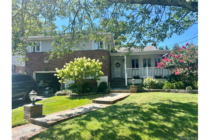 Split level home with brick siding, a front yard, covered porch, and an attached garage