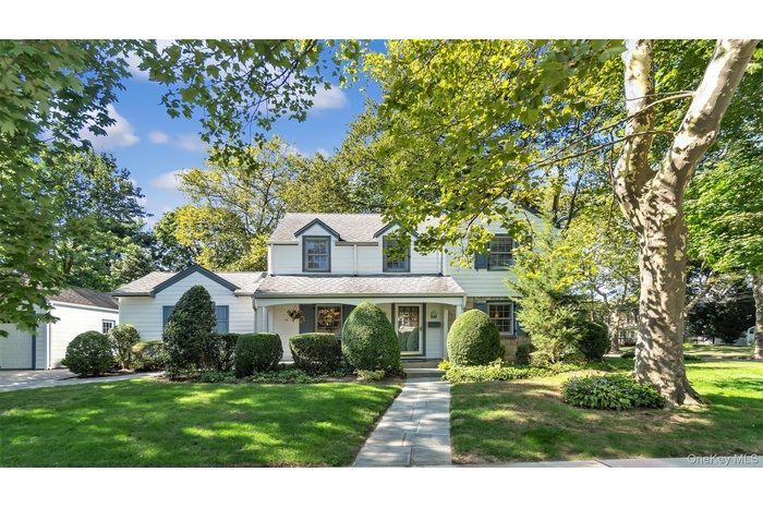 Traditional-style house with a porch, a front yard, a shingled roof, and a garage