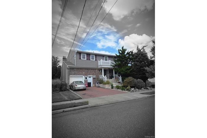 View of front of property featuring decorative driveway, a garage, a balcony, and stone siding