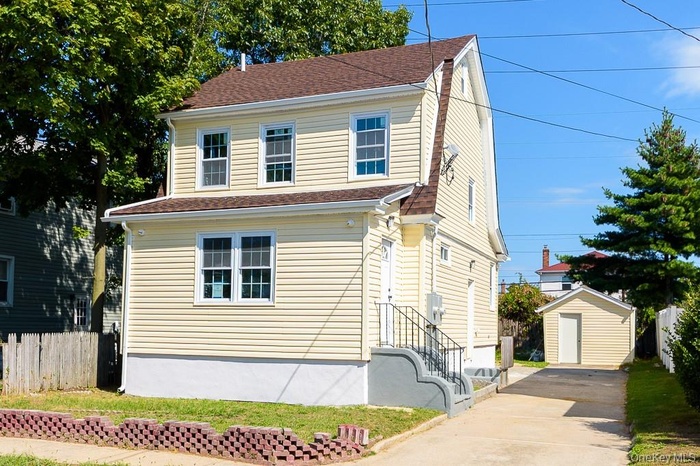 View of front of property featuring roof with shingles, a storage unit, and driveway