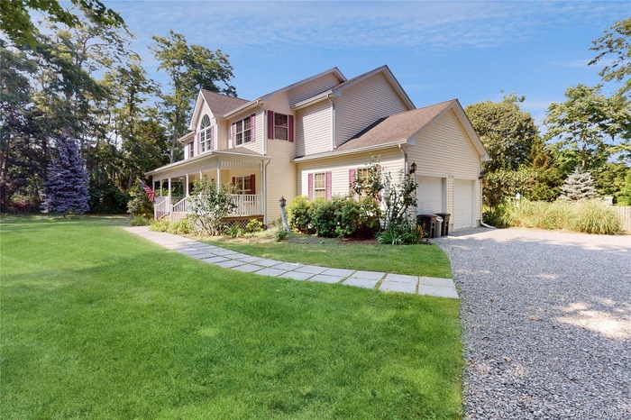 View of front facade with a front yard, covered porch, gravel driveway, and an attached garage