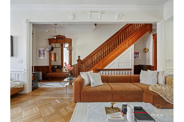 Living room featuring ornamental molding, wainscoting, a decorative wall, and stairs