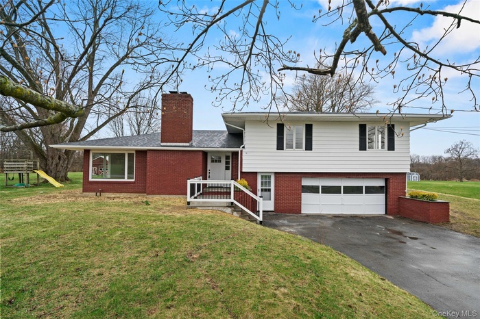 Split level home featuring brick siding, a garage, driveway, and a chimney