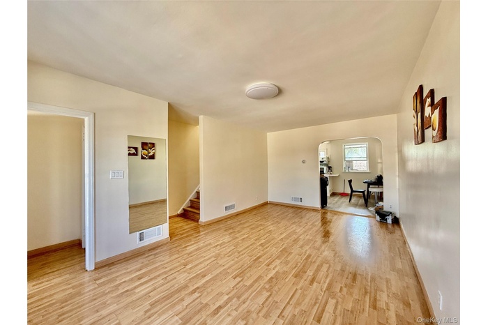 Unfurnished living room featuring light wood-style floors, arched walkways, and stairs