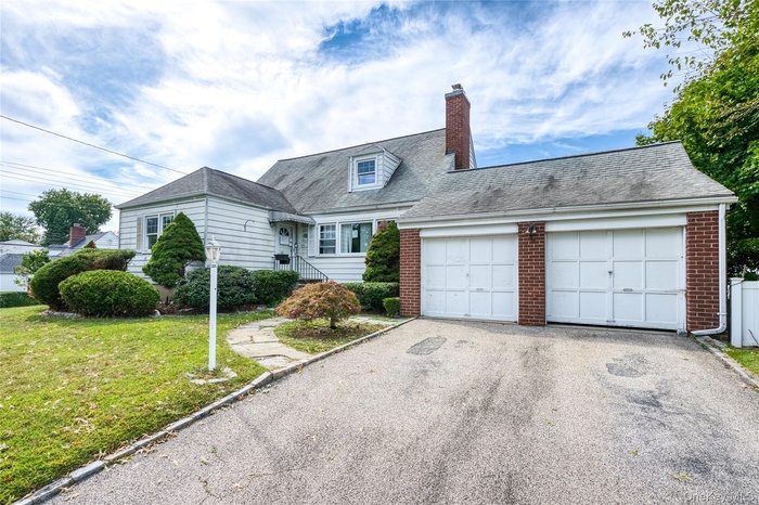 View of front of home featuring brick siding, driveway, roof with shingles, a chimney, and a front lawn
