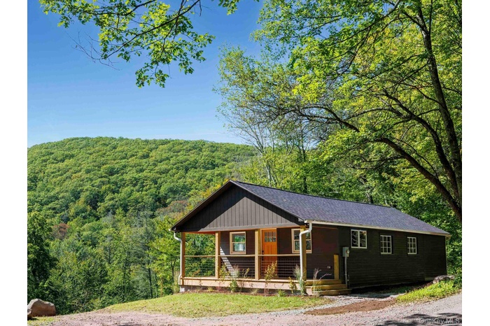 View of front of home with a wooded view, covered porch, a shingled roof, and board and batten siding