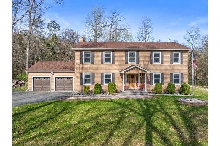 Colonial house with an attached garage, a chimney, a front yard, and aphalt driveway