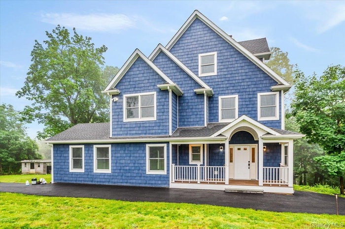 Shingle-style home featuring a porch, a front lawn, and roof with shingles