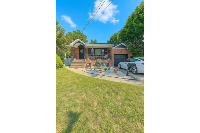 Single story home featuring a porch, brick siding, a garage, a front yard, and driveway