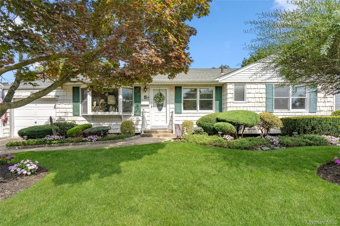 View of front facade featuring a front yard, a shingled roof, and a garage