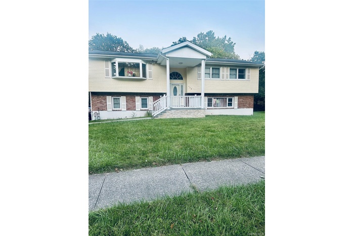 Raised ranch with brick siding, covered porch, and a front yard
