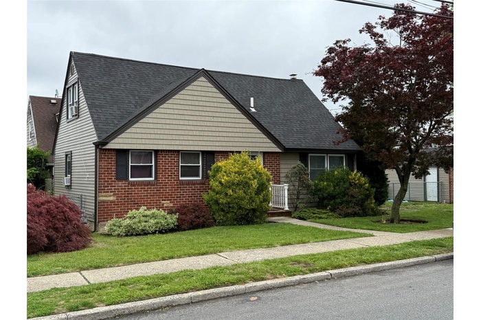 View of front facade featuring brick siding, a front yard, and a shingled roof