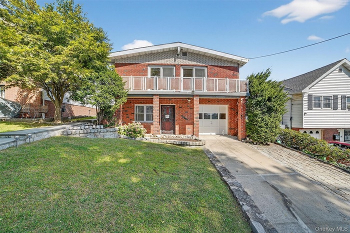 View of front of property with brick siding, concrete driveway, a front yard, a garage, and a balcony