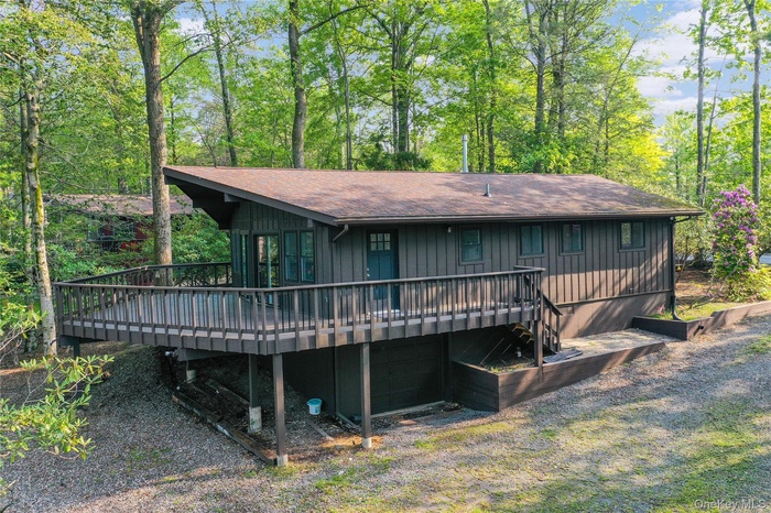 Back of property with a wooden deck, roof with shingles, and a garage