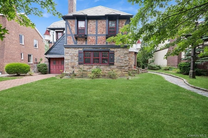 Tudor home featuring stone siding, a front yard, a garage, and a chimney