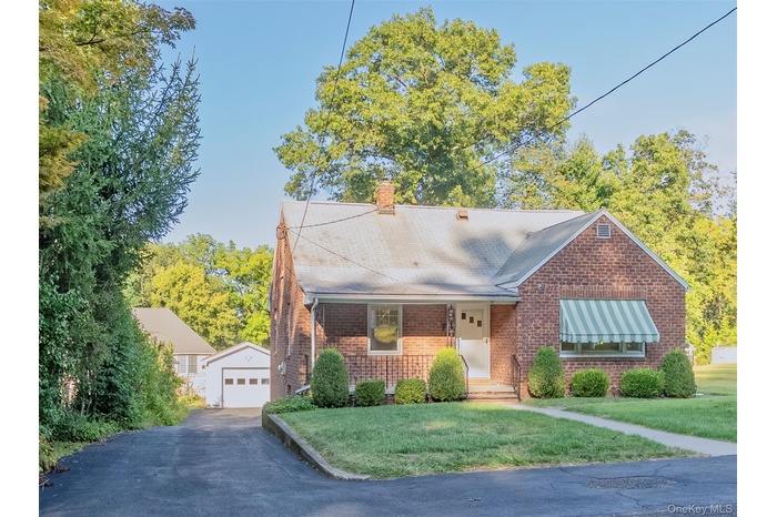 View of front of house featuring an outdoor structure, a front lawn, a chimney, a garage, and brick siding