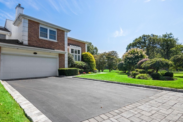 Traditional-style home with brick siding, driveway, a front lawn, an attached garage, and a chimney