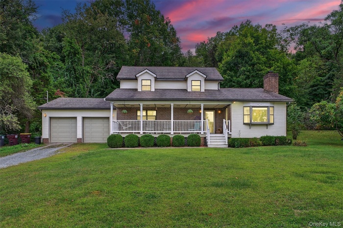View of front of home with a porch, driveway, a front yard, a chimney, and an attached garage