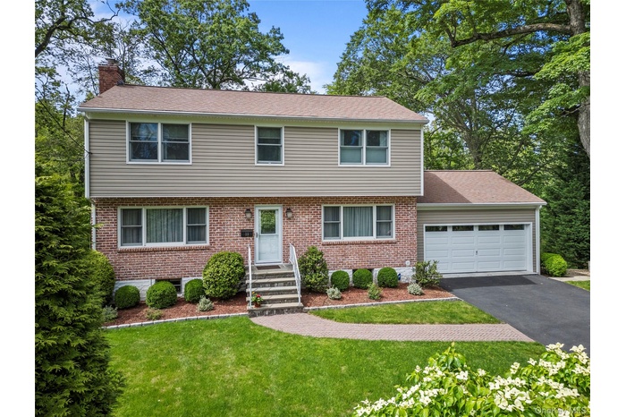Colonial house featuring a garage, asphalt driveway, a chimney, a front lawn, and brick siding