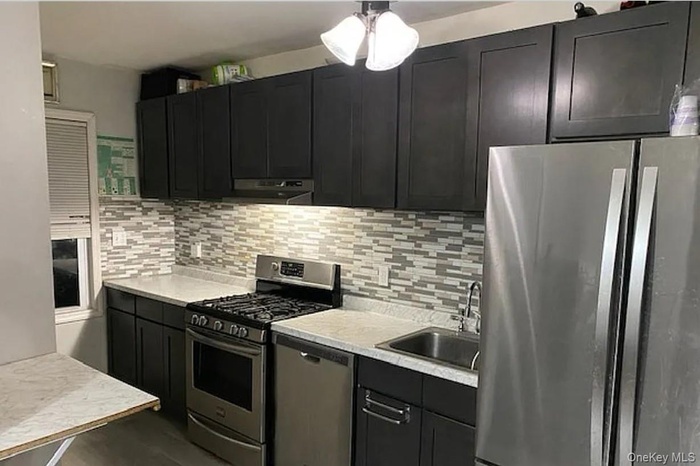 Kitchen featuring appliances with stainless steel finishes, dark cabinetry, light countertops, and tasteful backsplash