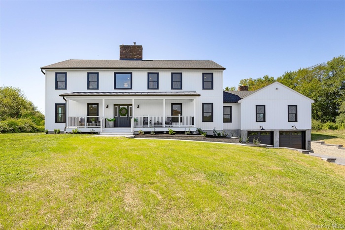 Front view of house featuring covered porch, a chimney, an attached garage, and a yard