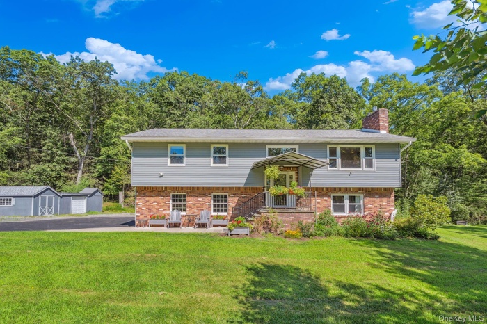 Split foyer home with brick siding, a storage unit, a front lawn, and a chimney
