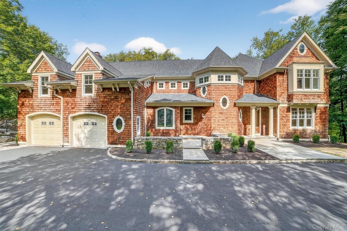 Shingle-style home featuring asphalt driveway, a shingled roof, an attached garage, and a chimney