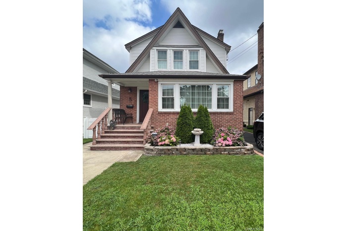 View of front facade with a front yard, brick siding, a chimney, and a porch
