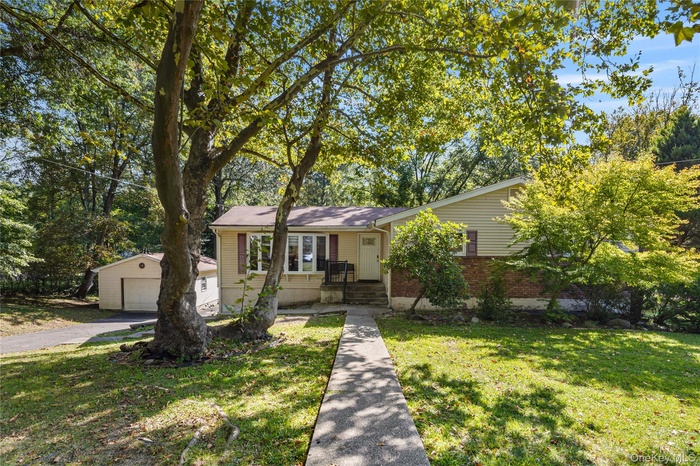 View of front of house with an outbuilding, a front yard, a detached garage, and view of wooded area