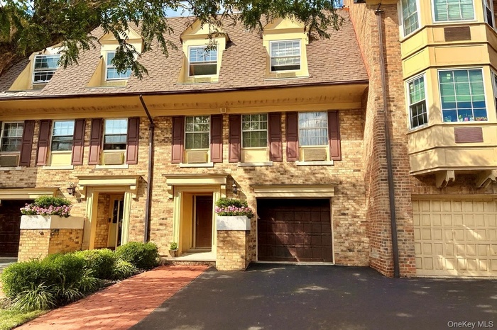 View of front of property with an attached garage, driveway, a shingled roof, and brick siding