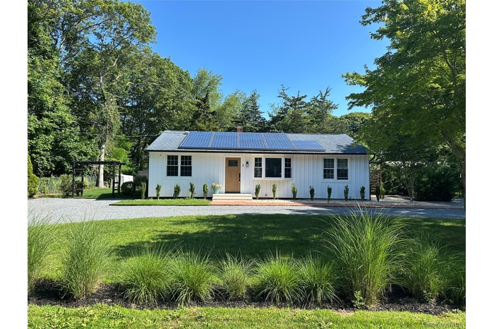 View of front of house with covered porch, a chimney, board and batten siding, and roof mounted solar panels