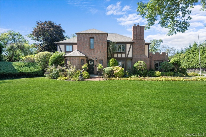 Back of house featuring a chimney, a lawn, brick siding, and roof with shingles