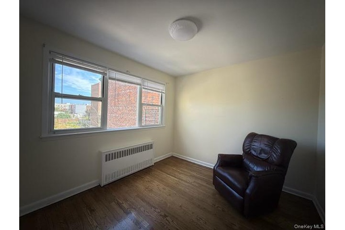 Living area with radiator heating unit and dark wood-style floors