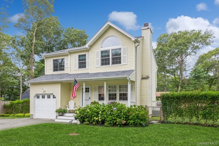 Traditional-style house with a front lawn, aphalt driveway, a porch, a garage, and a chimney