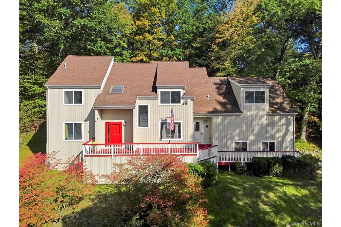View of front of home with a shingled roof, a front yard, and view of scattered trees