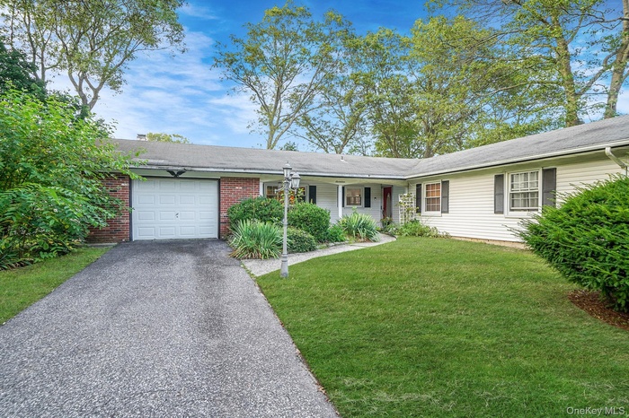 Ranch-style home with asphalt driveway, an attached garage, a front lawn, brick siding, and a porch