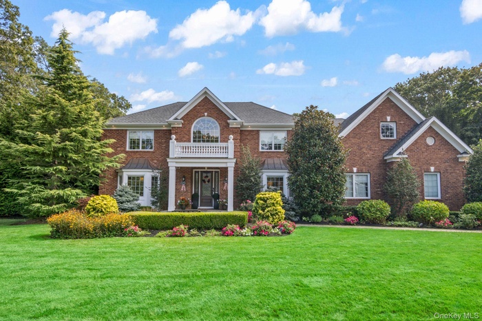 Colonial house with brick siding, a front yard, and a balcony