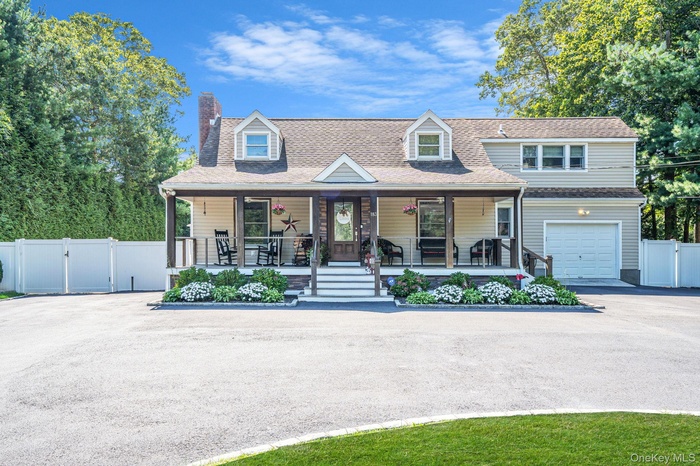 New england style home featuring a gate, a porch, a chimney, a garage, and driveway